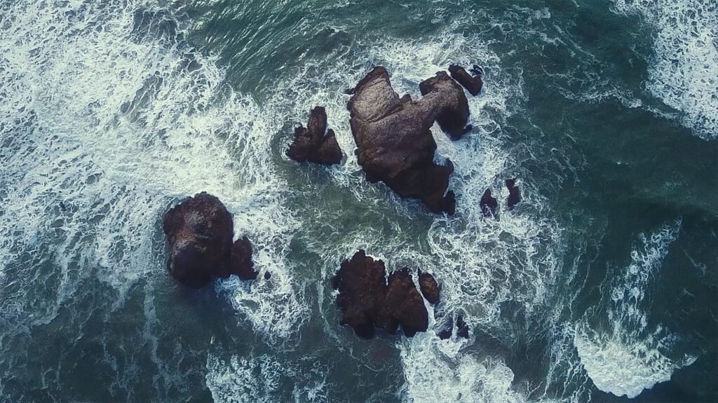 Dynamic aerial view of ocean waves crashing against rocky structures, captured from above.