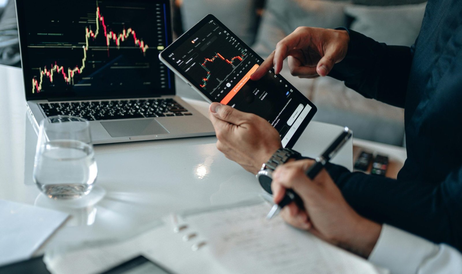 Business professionals reviewing financial charts on digital devices in a modern office setting.